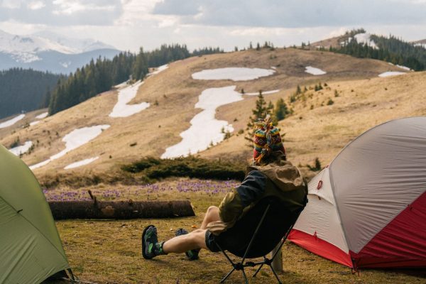 a person sitting on a chair outside by a tent and a lake