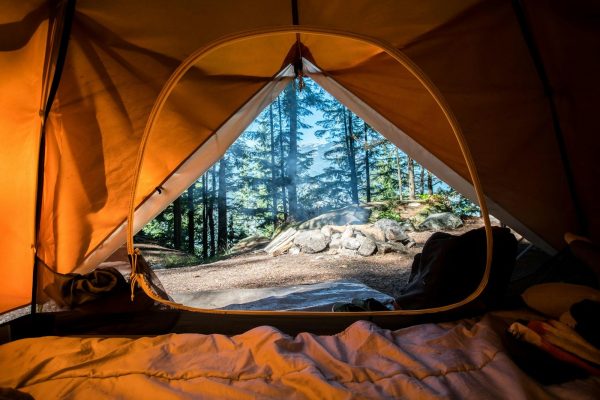 Summer campsite with a tent, chairs and warm lights among trees
