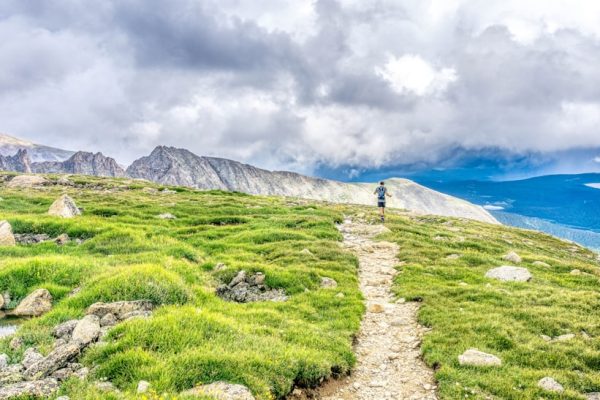 Two hikers with backpacks walking along a trail toward snow-capped mountains