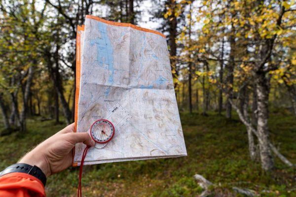 A person in a beanie holding a compass against a blurred mountain landscape