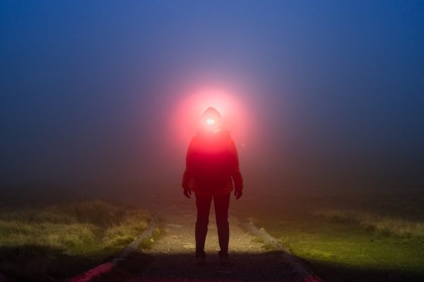 woman standing holding flashlight into woods