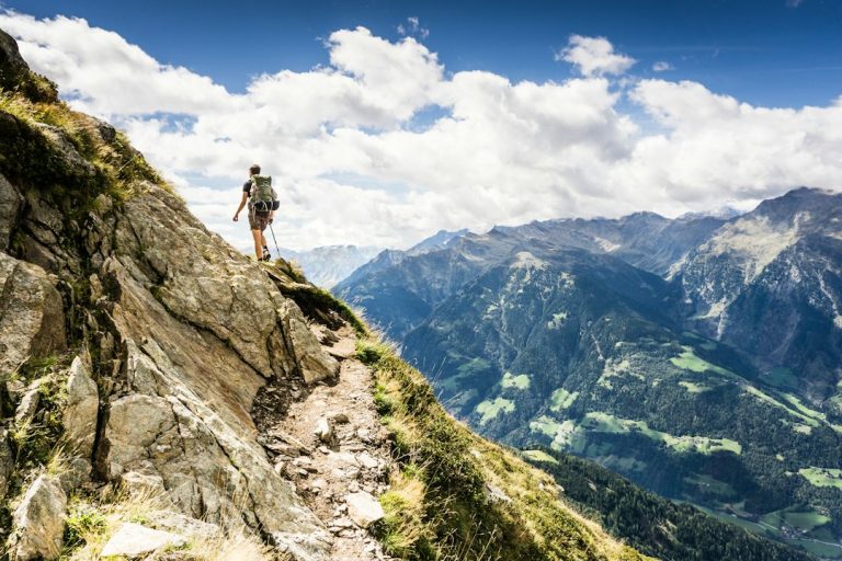 Two hikers with backpacks walking along a trail toward snow-capped mountains