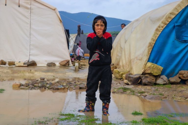 Child standing in flooded camp with tents behind tents