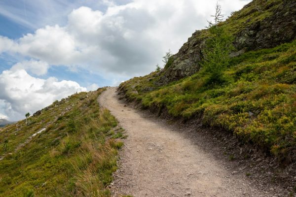Two hikers with backpacks walking along a trail toward snow-capped mountains